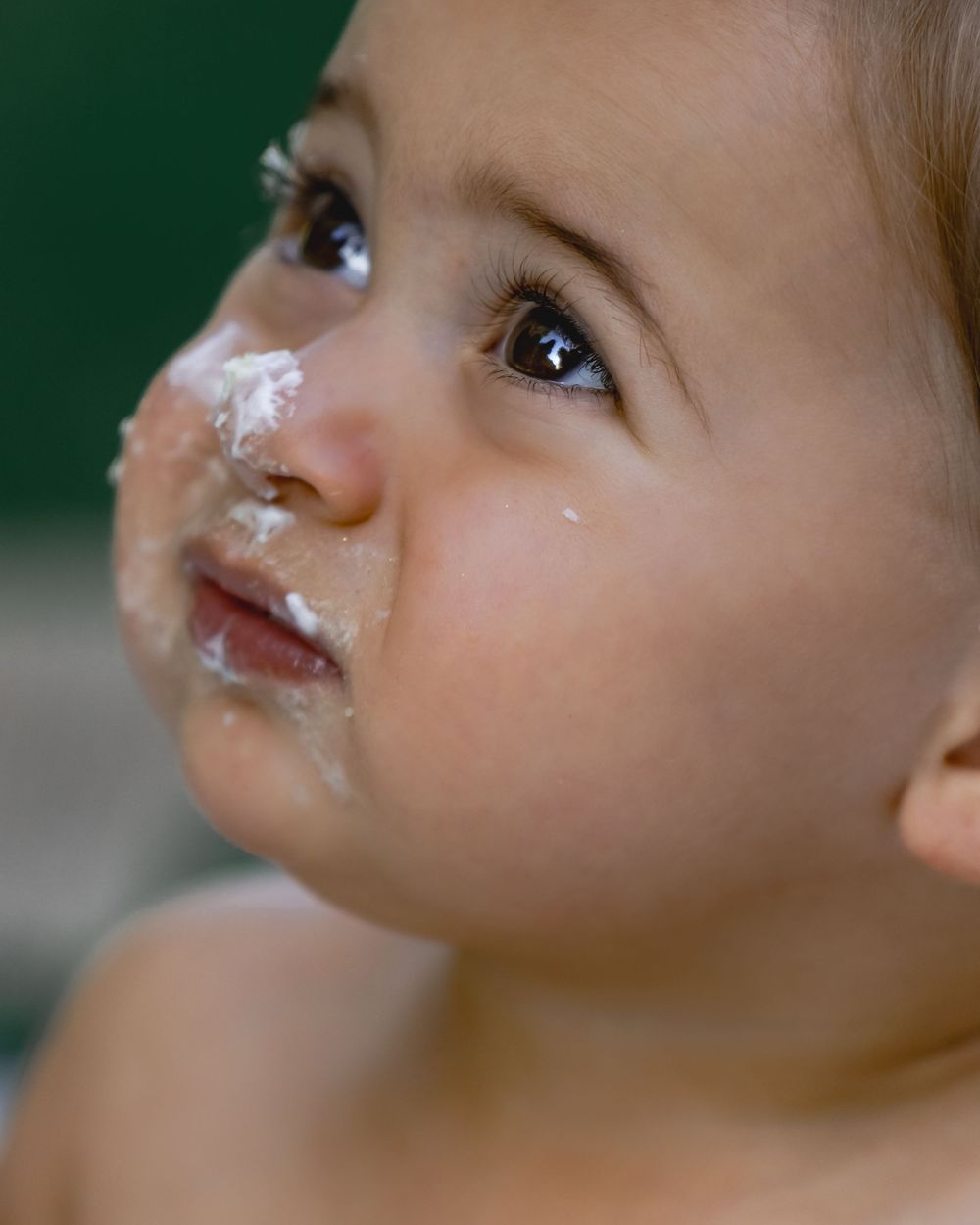 Close-up of baby with white frosting on nose and face looking upward.