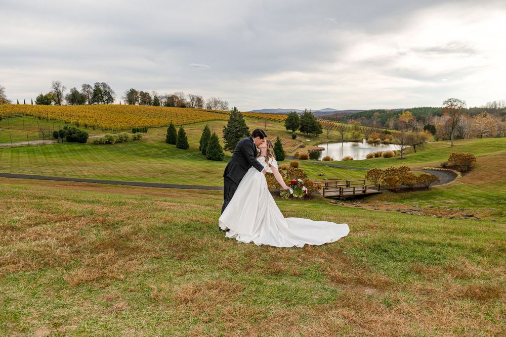 Panoramic view of a rustic outdoor wedding ceremony setup in a rolling green countryside with white chairs and decor.