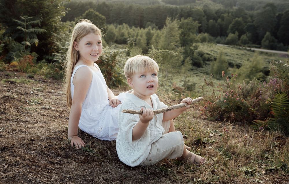 Brother and sister sitting during an outdoor golden hour shoot smiling with to their parents.  The little boy has found a stick to play with
