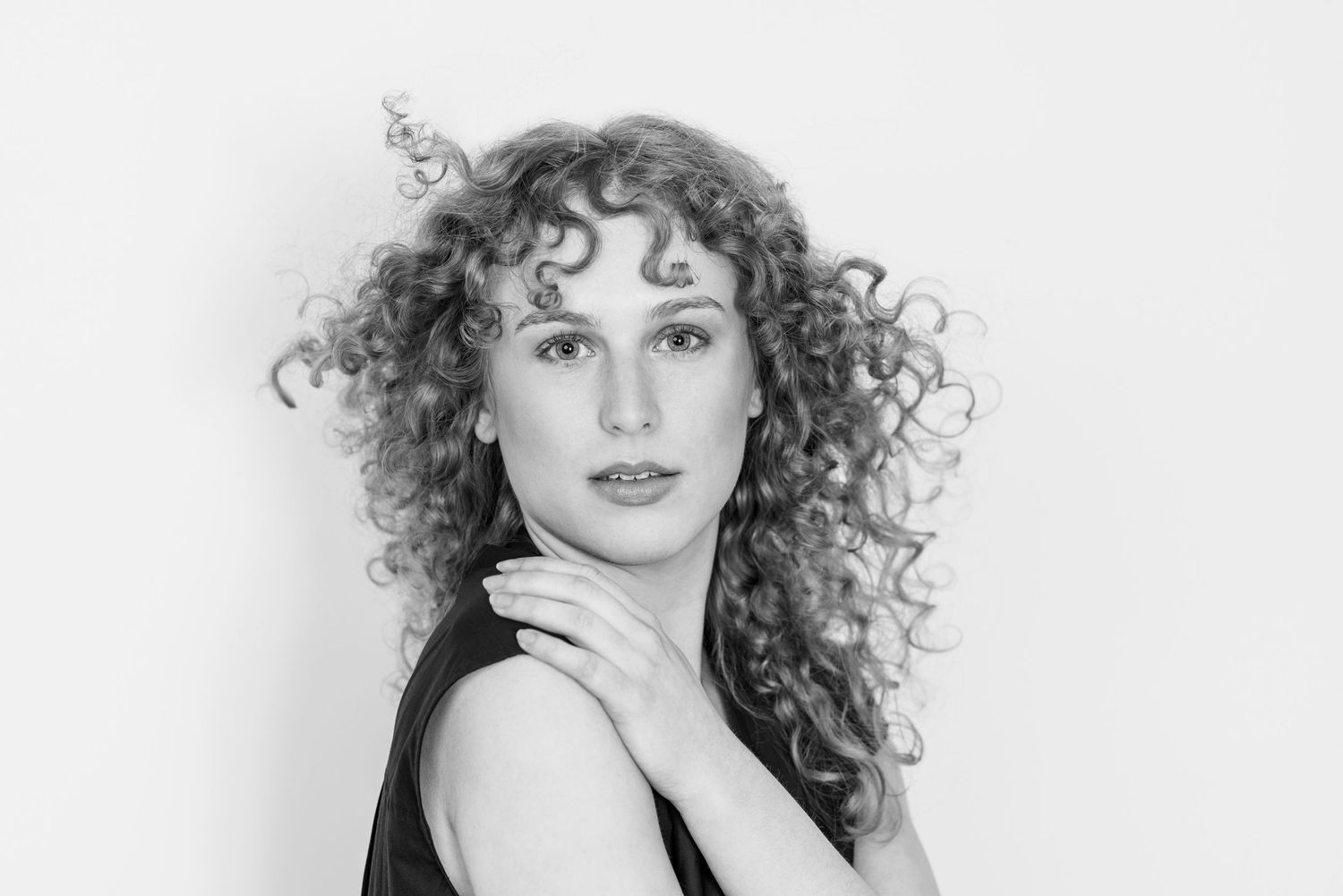 A series of three professional headshots showing a person with curly blonde hair in a black top against a light background.
