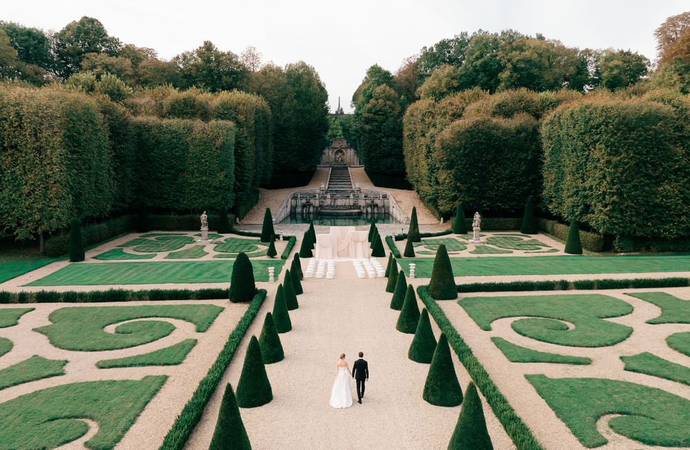 Aerial panoramic view of formal French gardens with manicured hedges, geometric patterns, and walking paths.