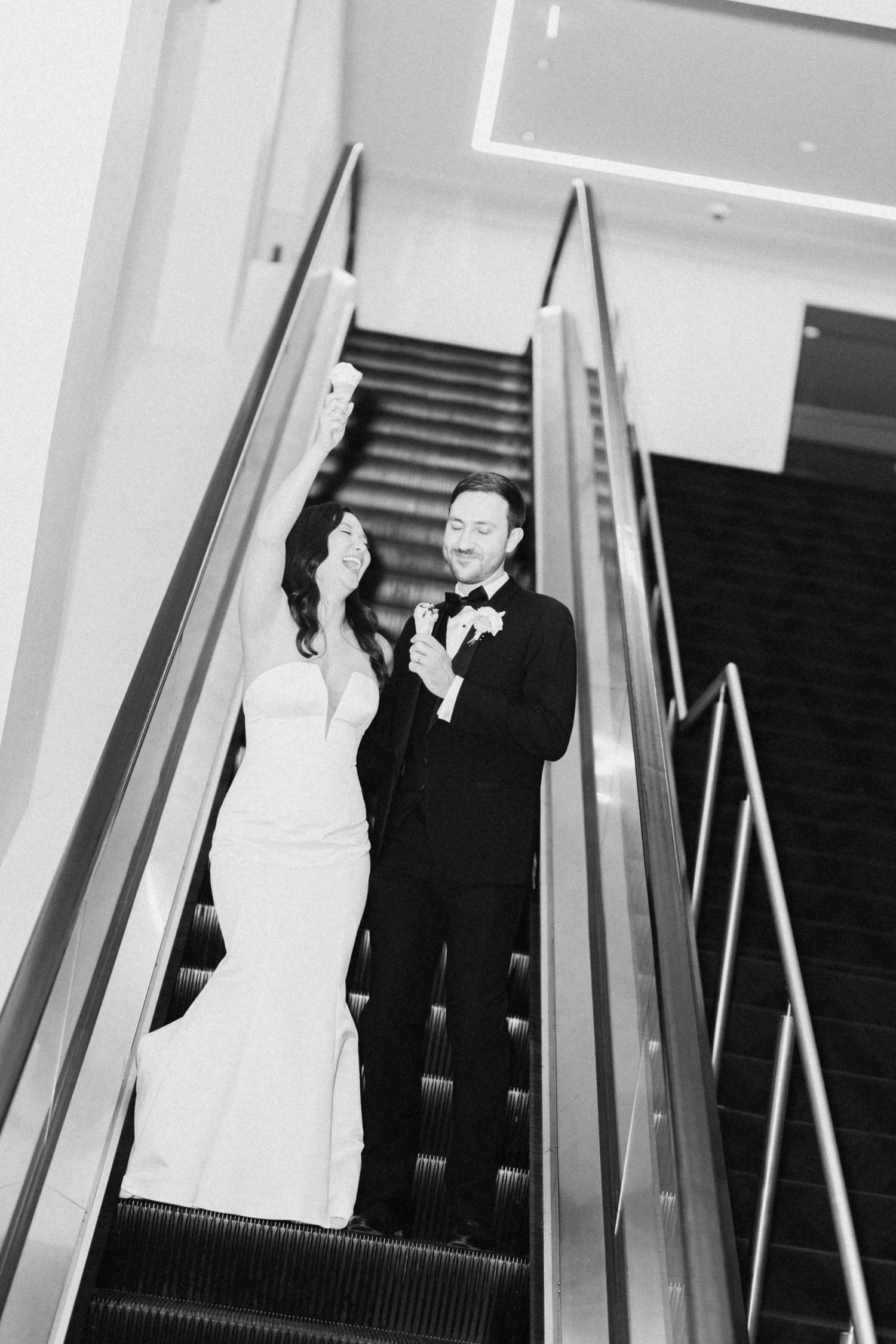 Black and white photo of a bride and groom riding an escalator together on their wedding day.