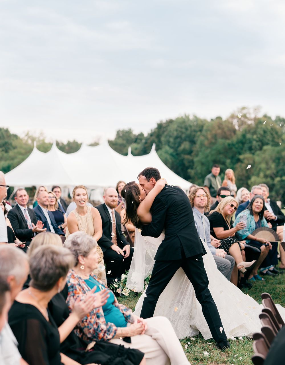 A panoramic view of wedding guests gathered outdoors under white tents during a celebration.