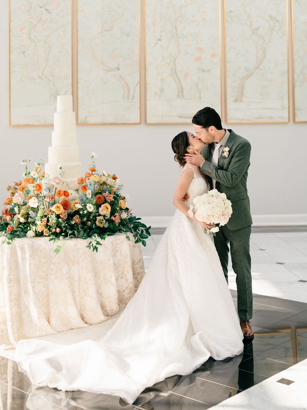Elegant wedding reception table with peach and white floral arrangements and champagne linens in a luxurious white room.