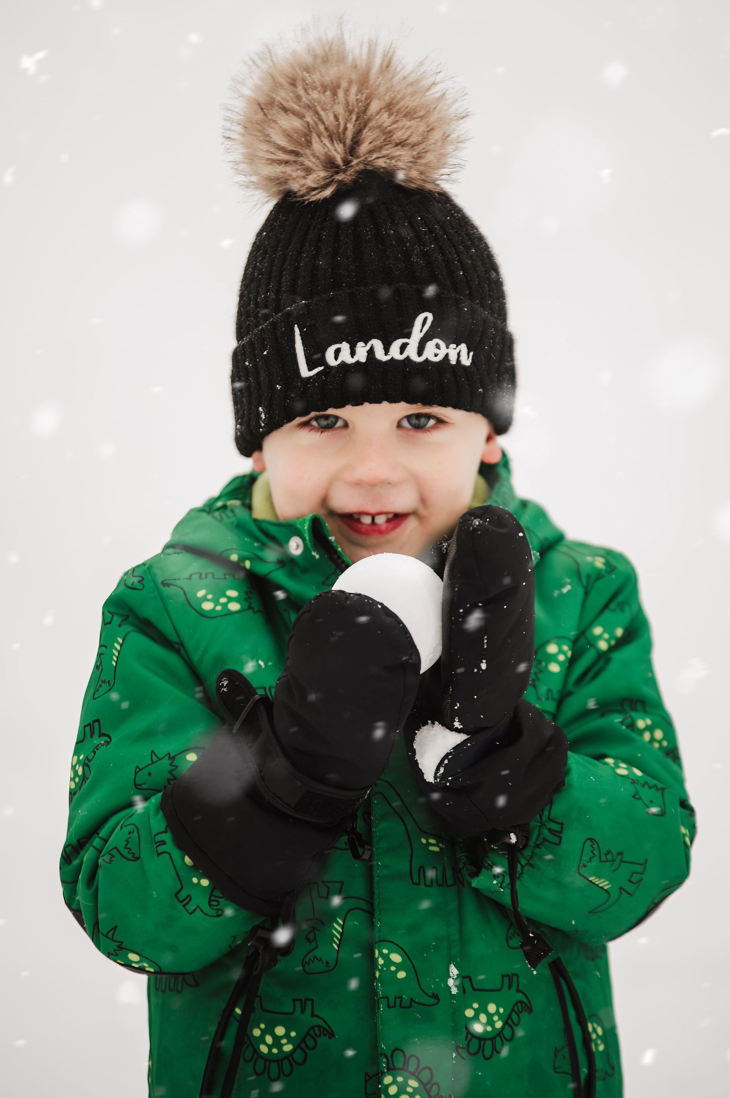 Winter portrait series showing playful moments in the snow wearing a green coat and pom pom hat.