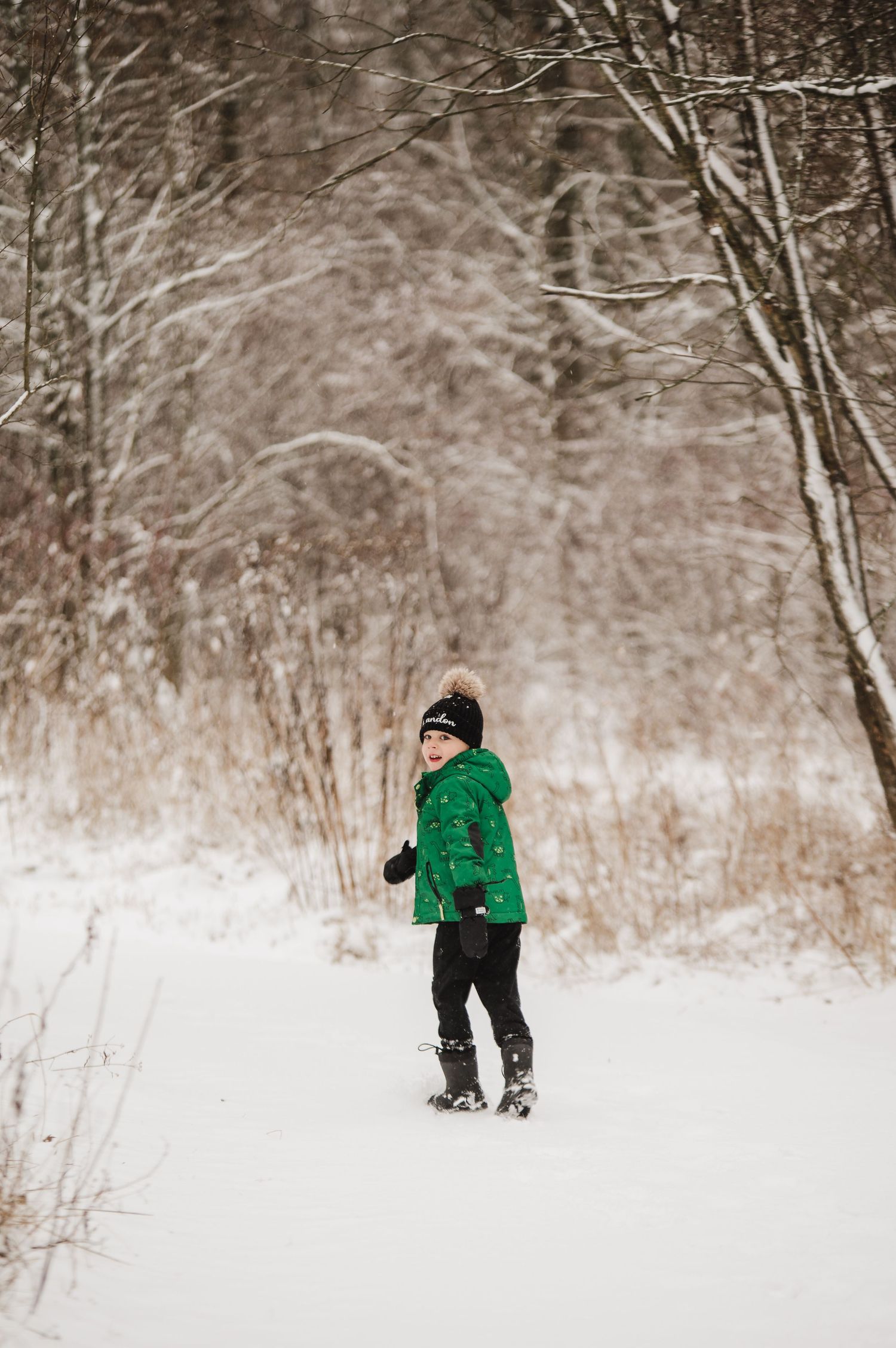 Person in bright green winter coat walking through snowy forest landscape.