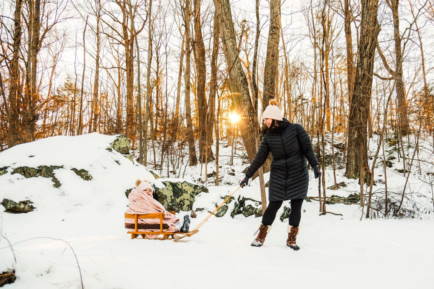 A snowy winter forest trail with bare trees and a wooden bench visible in the distance.