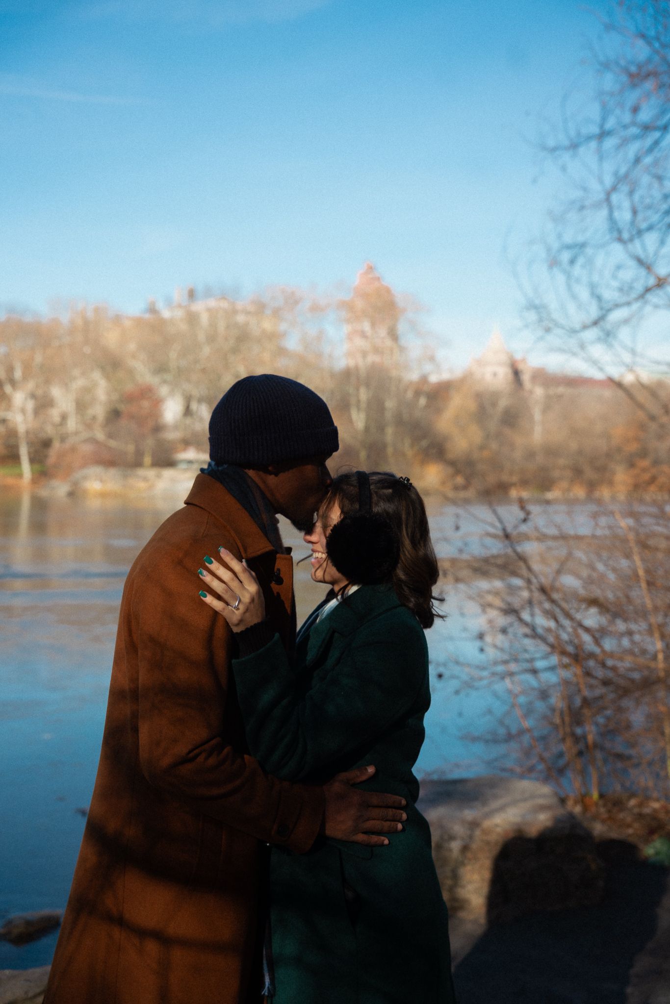 A couple shares a tender moment by a lake during golden hour.