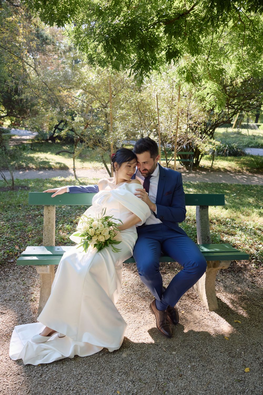 A couple shares an intimate moment on a wooden bench in a garden setting.