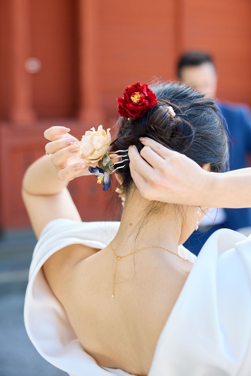 Close-up view of a bride's updo hairstyle adorned with red flowers against a terracotta wall.