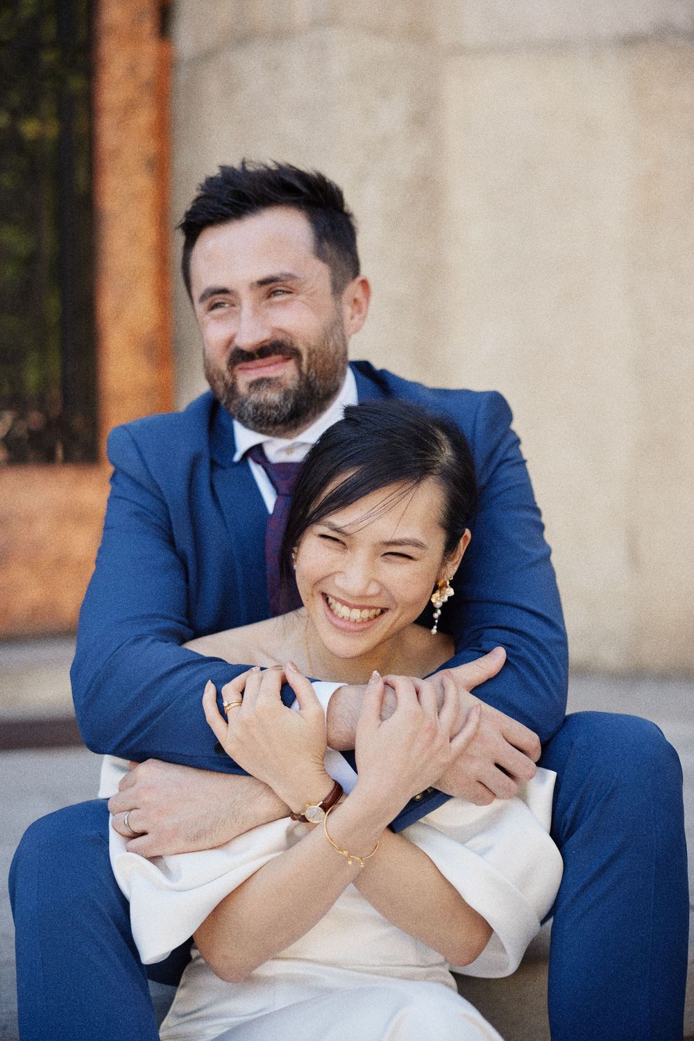 Joyful couple sharing a candid moment together outdoors against a textured wall.