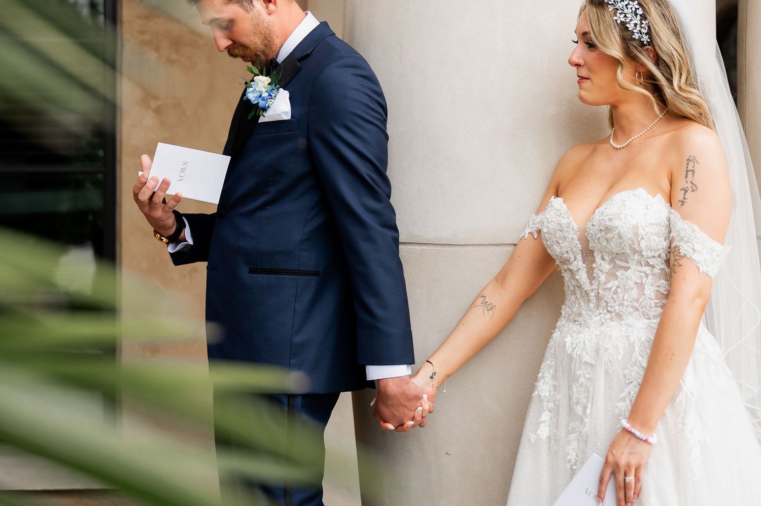 Bride in strapless lace gown shares first look with groom in navy suit near white columns.