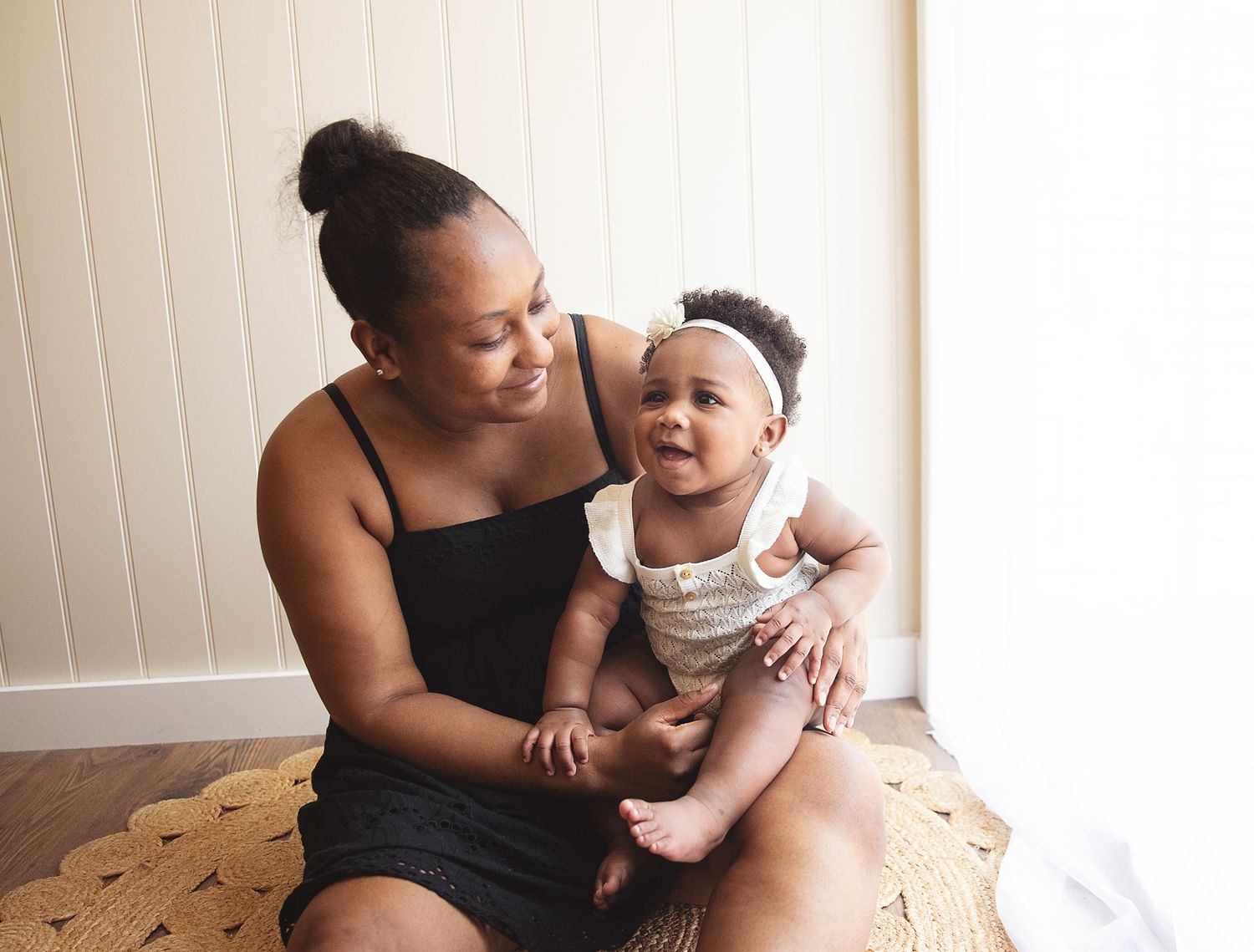 A tender moment between parent and baby sitting together on a wooden floor in a bright room. at a photoshoot in Sidcup