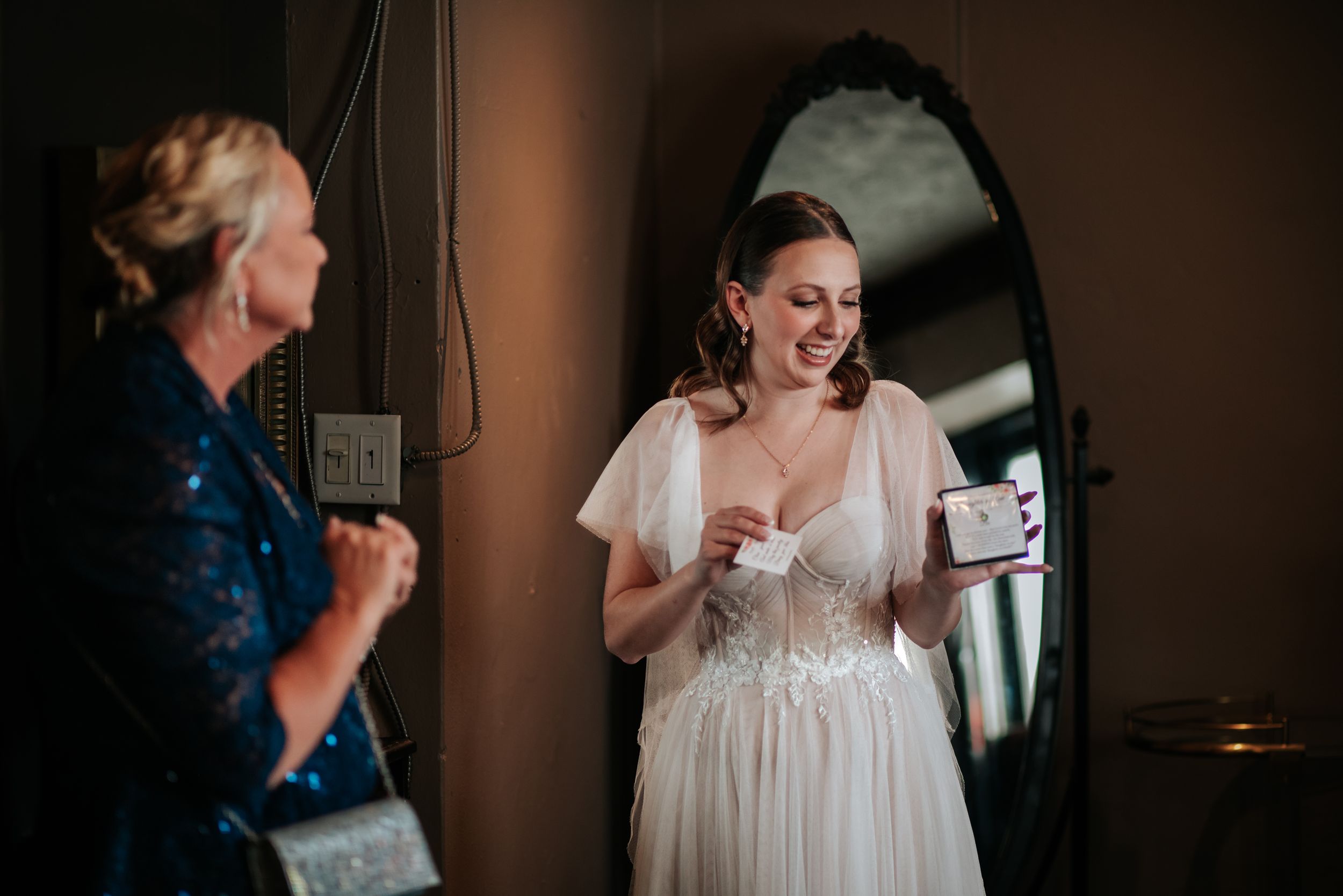 A bride in a flowing white dress laughs joyfully while getting ready for her wedding day.