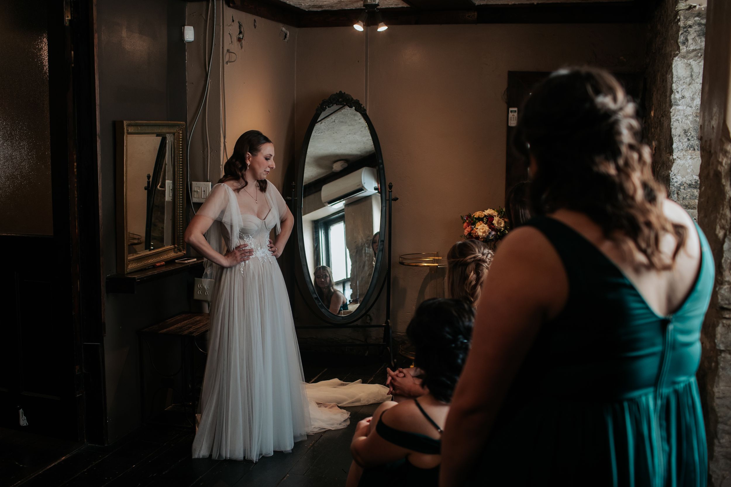 Wedding party getting ready in a dimly lit room with elegant dresses and preparations underway.