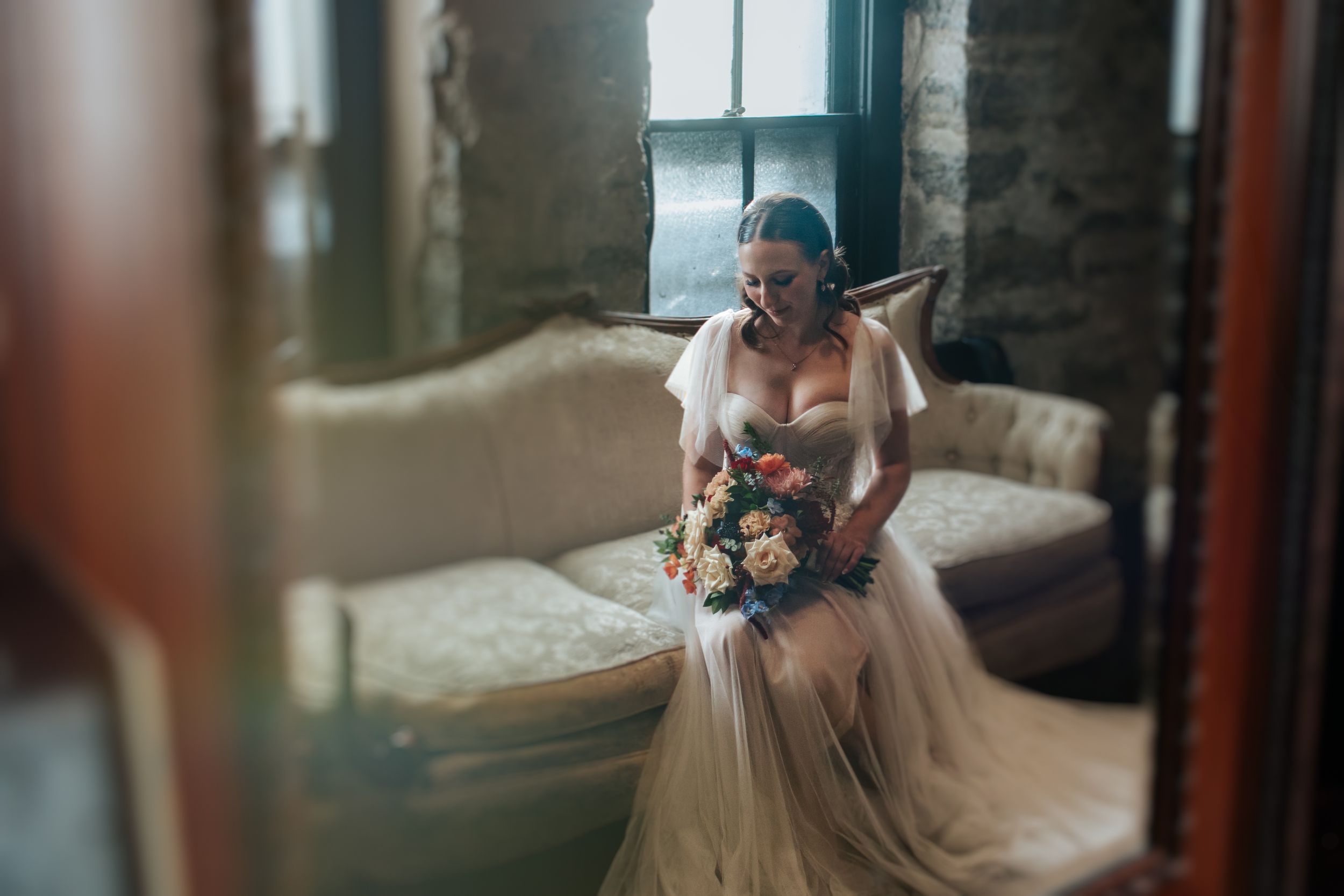 A couple shares a tender moment in a sunlit room wearing elegant wedding attire.