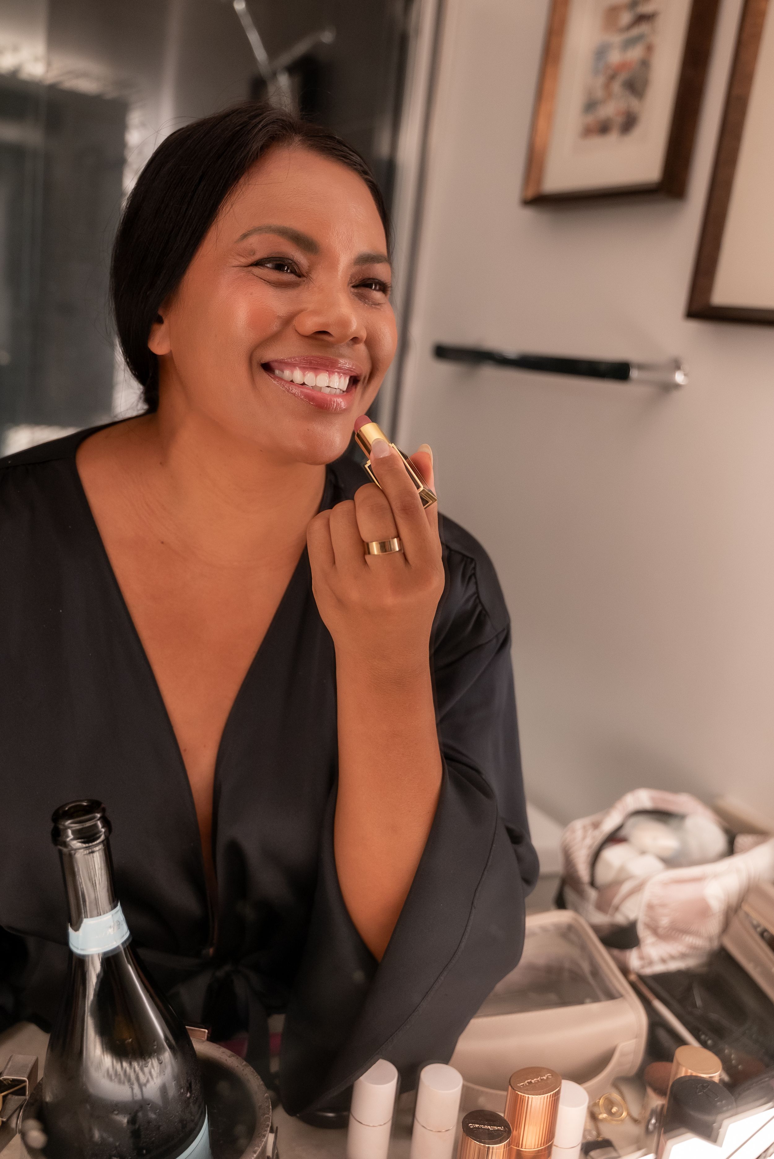 A person in a black top smiles warmly while sitting at a table with wine bottles and glassware.