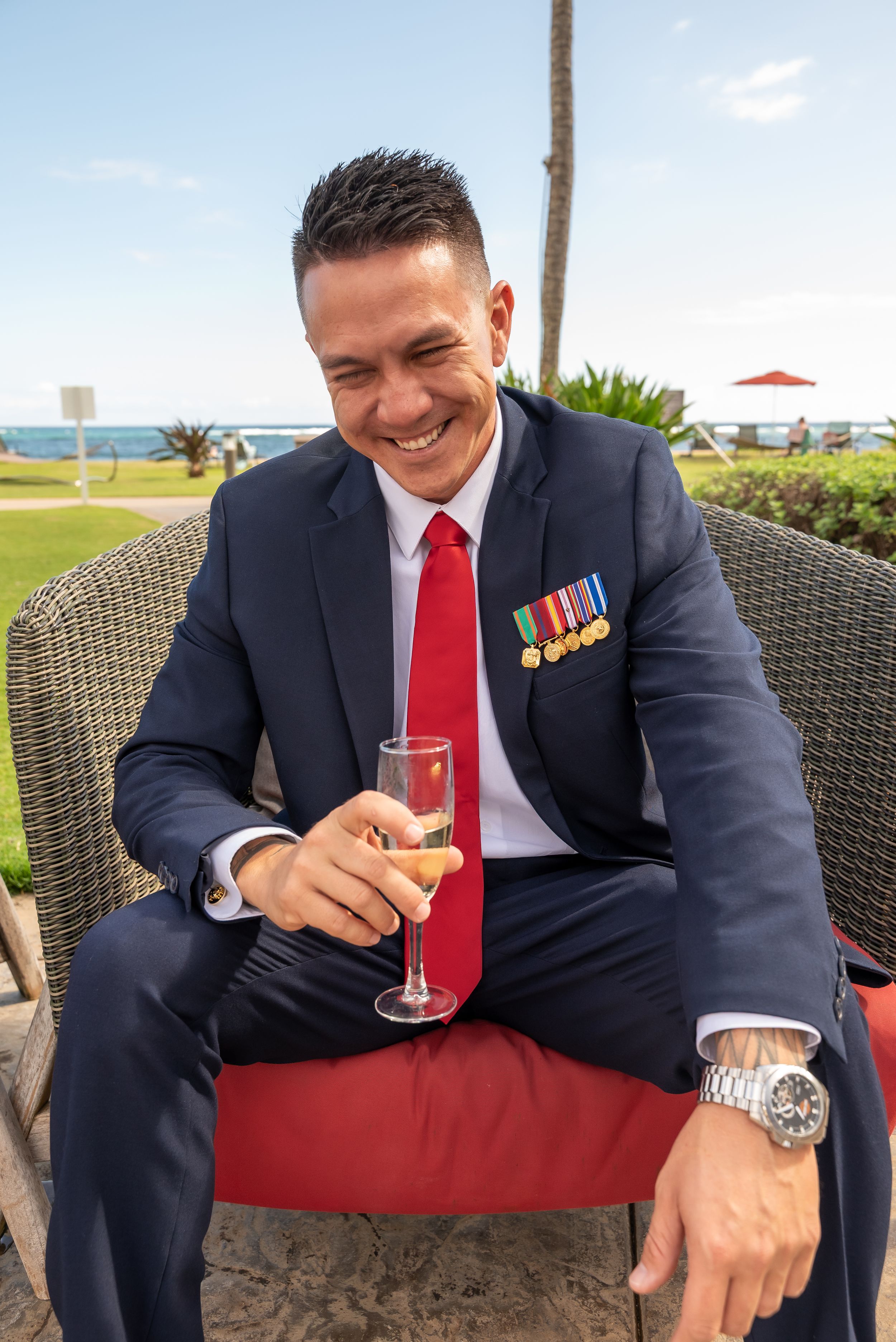 Military servicemember in dress uniform with medals smiles while holding champagne at outdoor celebration.