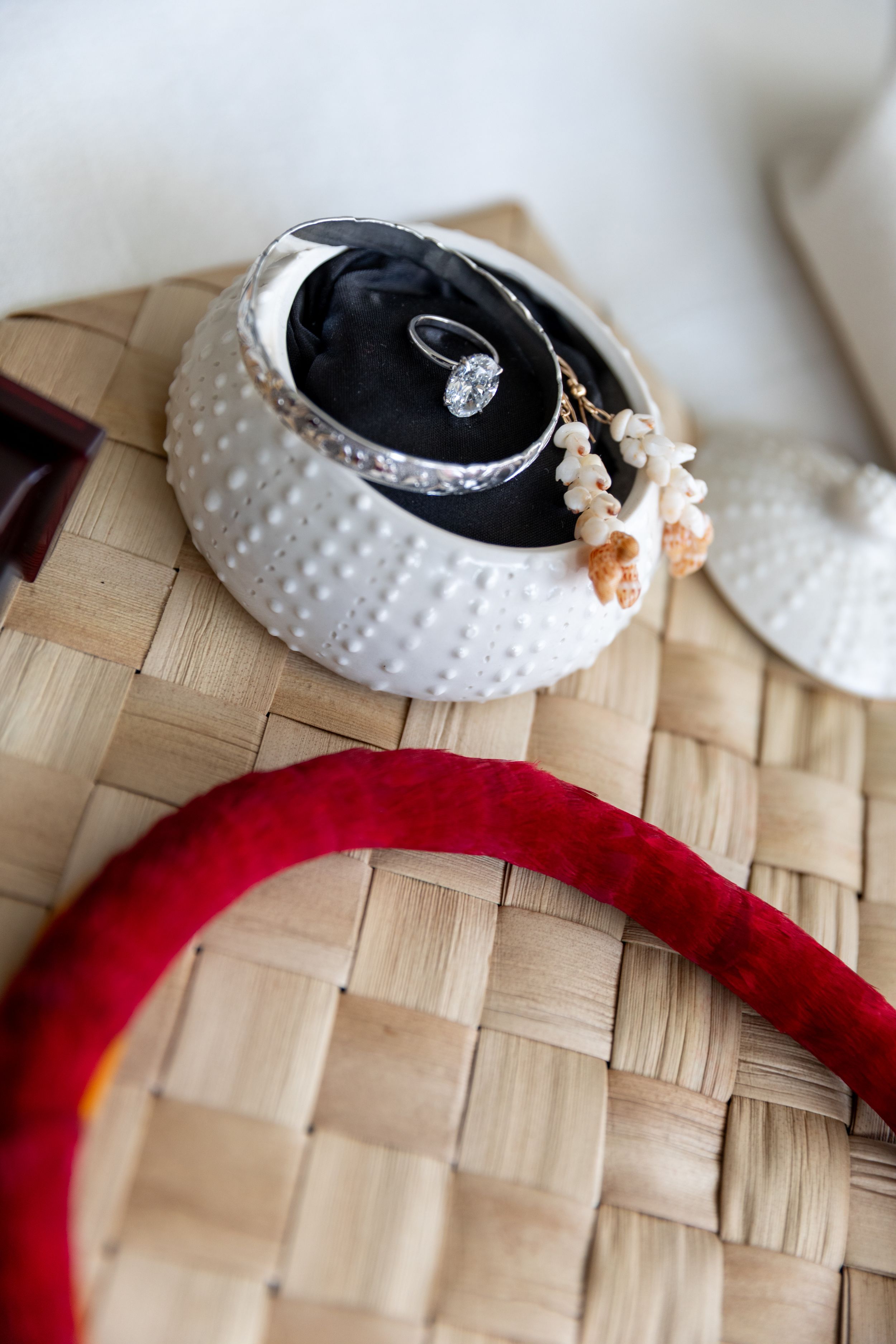 Close-up view of white pearl-studded wedding rings with delicate floral accents resting on a woven bamboo surface.