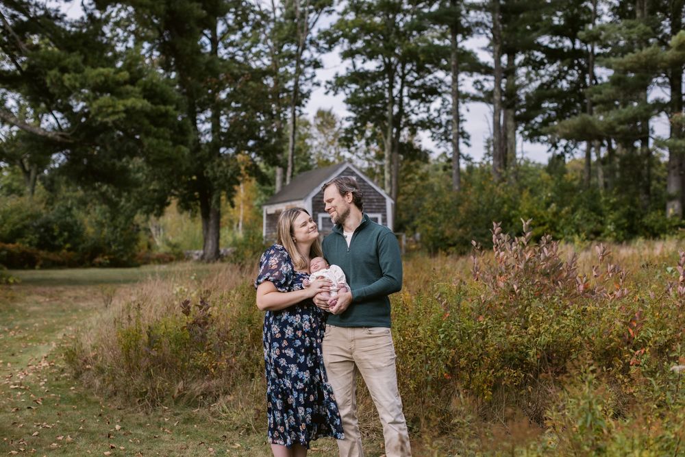 A husband and wife gaze at each other holding their newborn baby at a newborn shoot in Tamworth New Hampshire. Seacoast newborn photographer