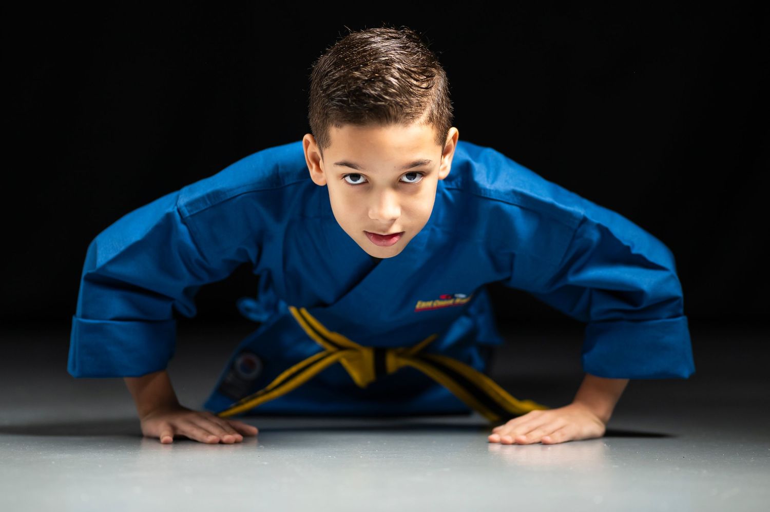 Studio photo of a young boy in martial arts clothes doing a push up