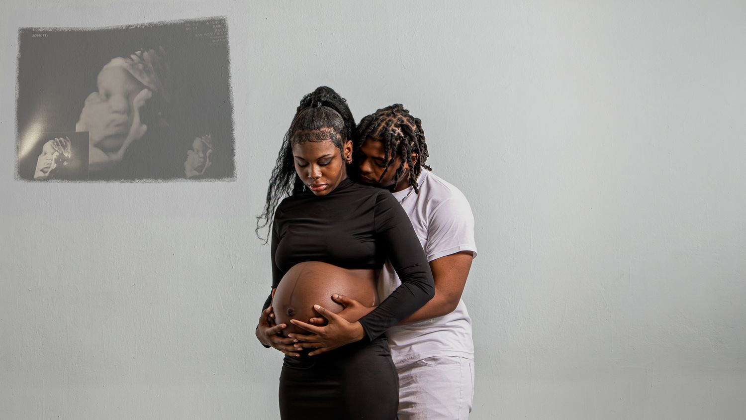 A tender maternity moment captured in black and white as a couple embraces, highlighting the pregnant belly.