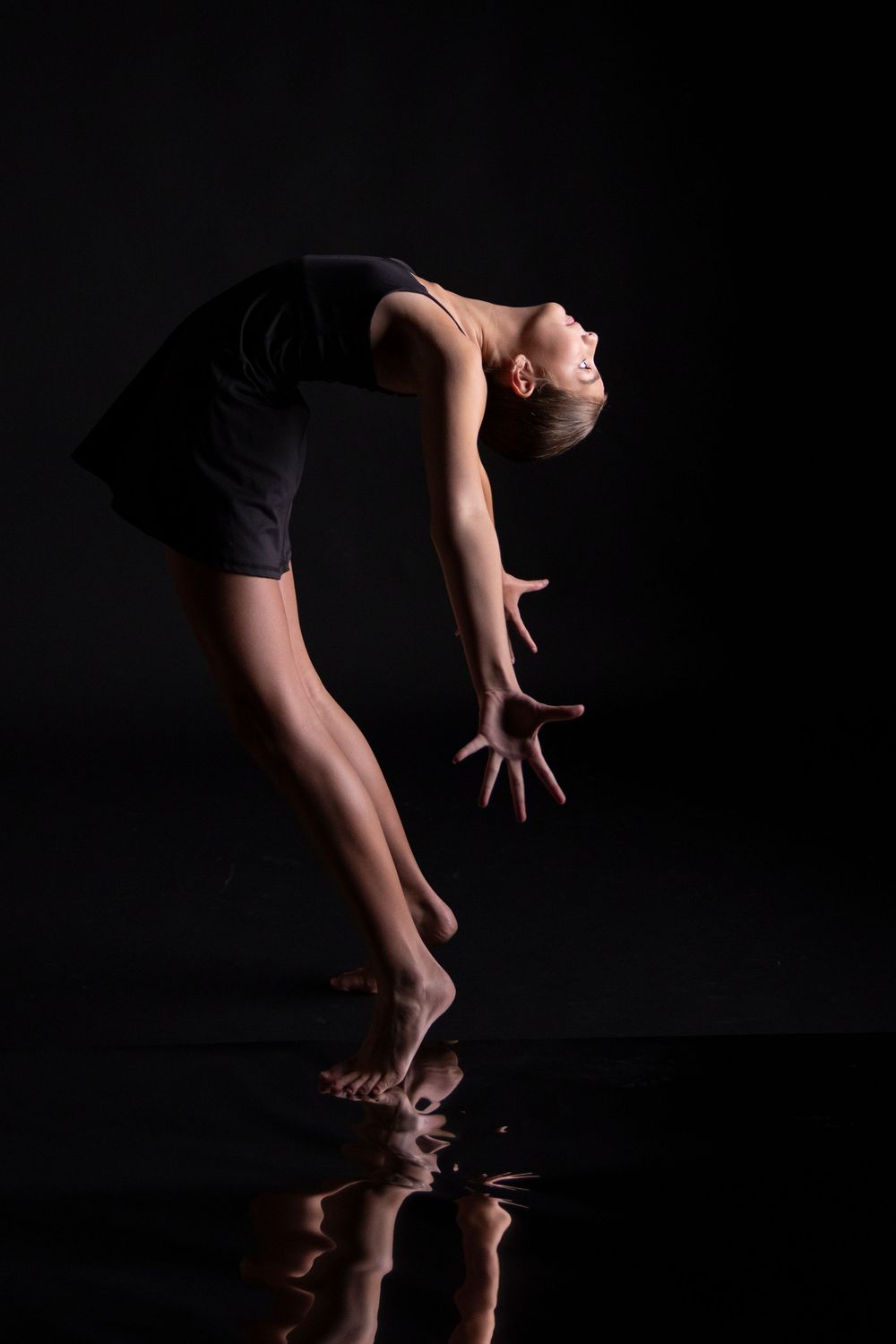 Dramatic silhouette of dancer arching backwards with reflection on dark floor.
