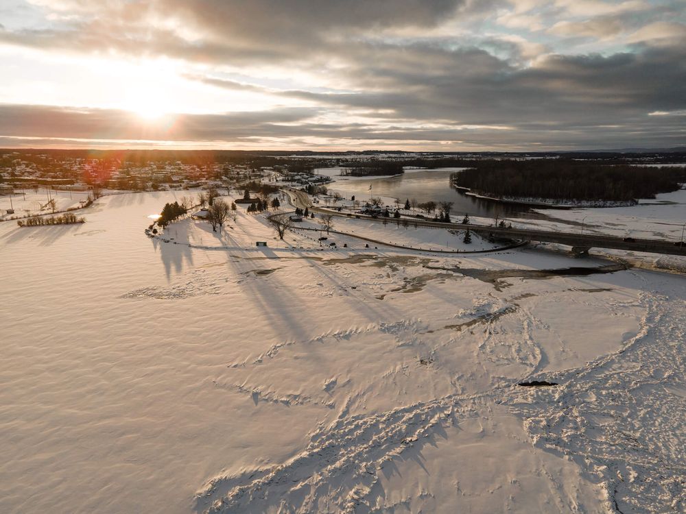Dramatic sunset sky over a snowy coastal landscape with boats visible in the distance.