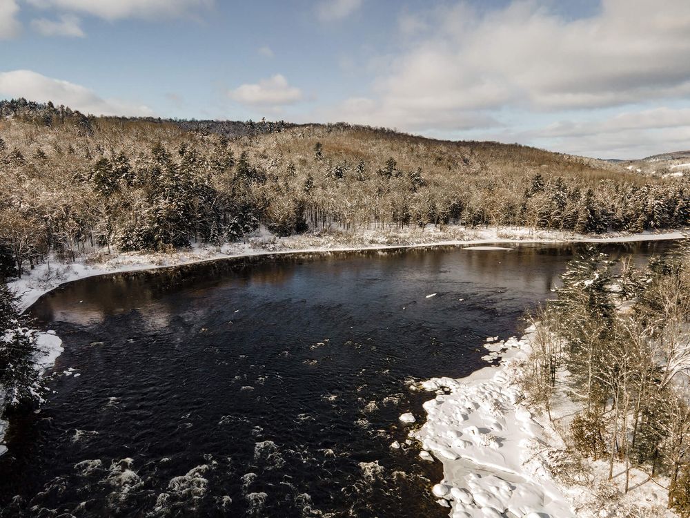 Panoramic winter vista of a lake surrounded by snow-dusted hills and forests.
