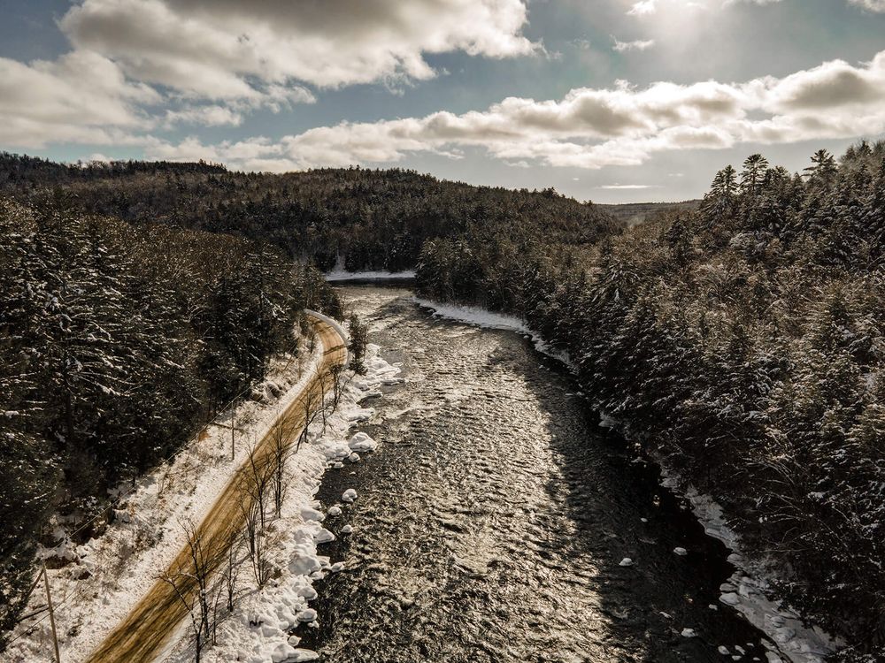Aerial panorama of a winding waterway through snow-covered landscape under cloudy skies.