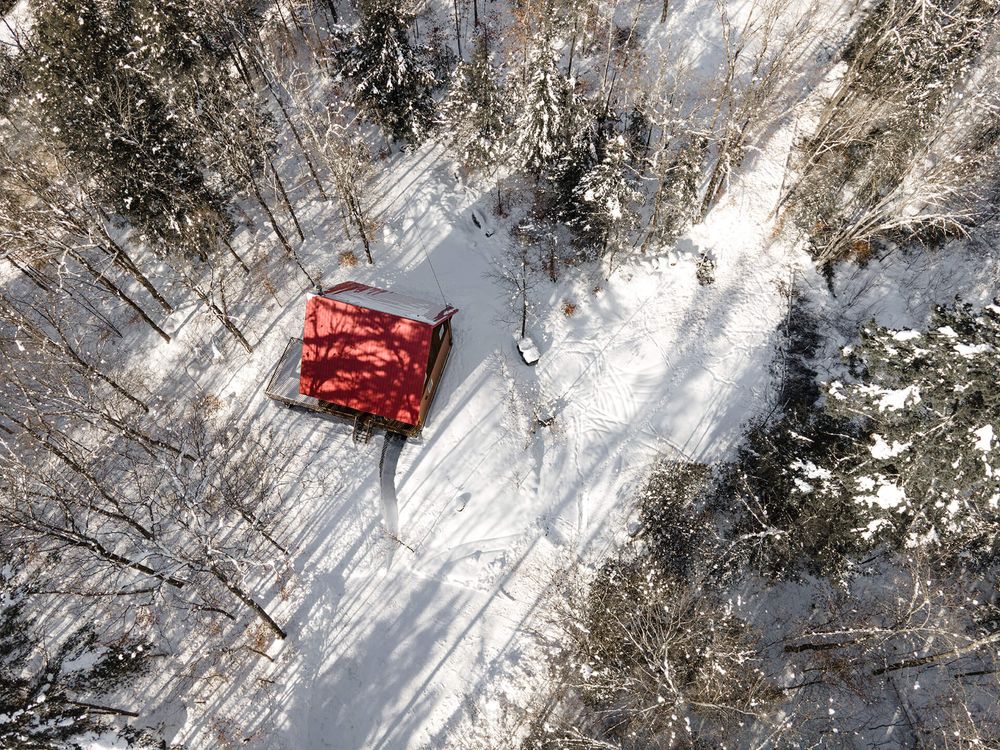 Aerial view of a red vehicle traveling along a snow-covered road near a river.