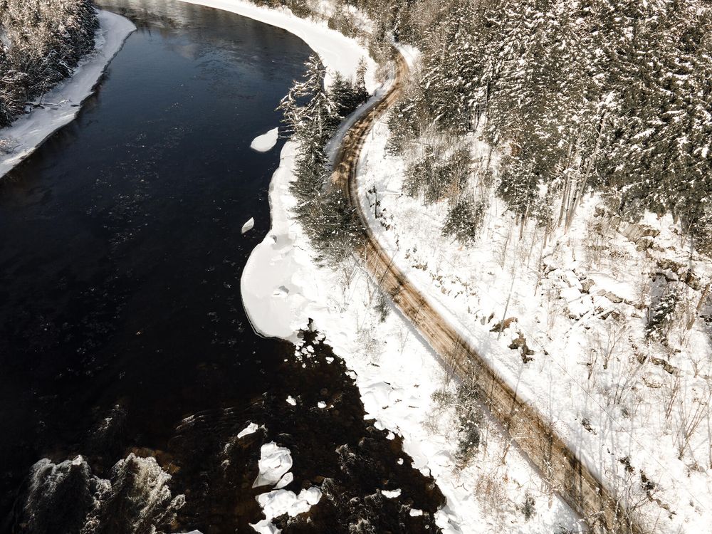 Meandering river cutting through snowy terrain with forest edges visible from aerial perspective.