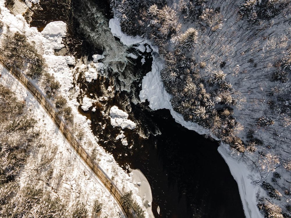 Snow-covered landscape with dark water and forested areas viewed from above.