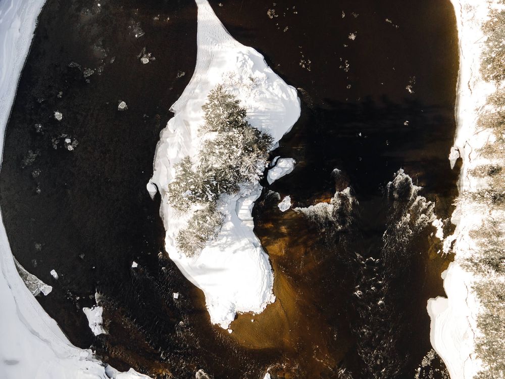 Aerial winter landscape showing a winding river through snow-covered terrain and dark forest.
