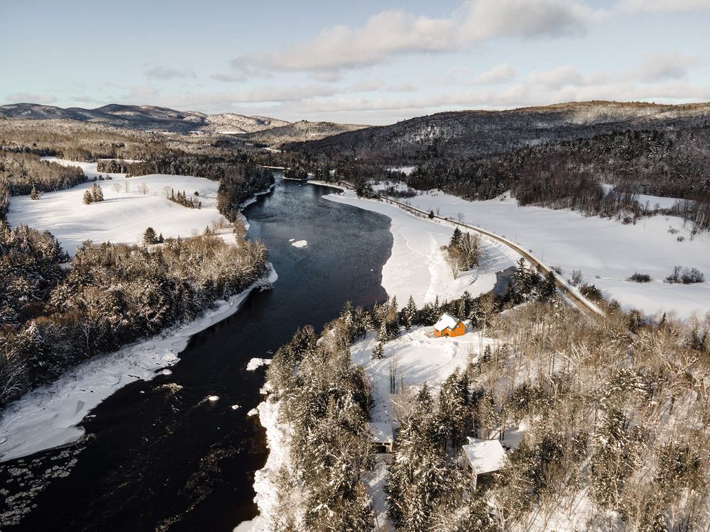 Panoramic winter vista of snow-covered hills and dark river winding through white landscape.