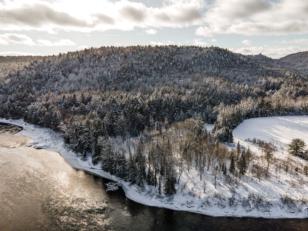 Winter aerial landscape showing snow-dusted forests and winding river through rugged terrain.
