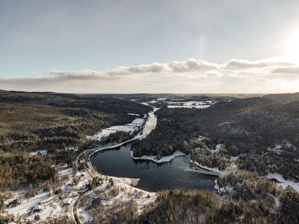 Snow-covered winter landscape with winding river through forested hills viewed from above.
