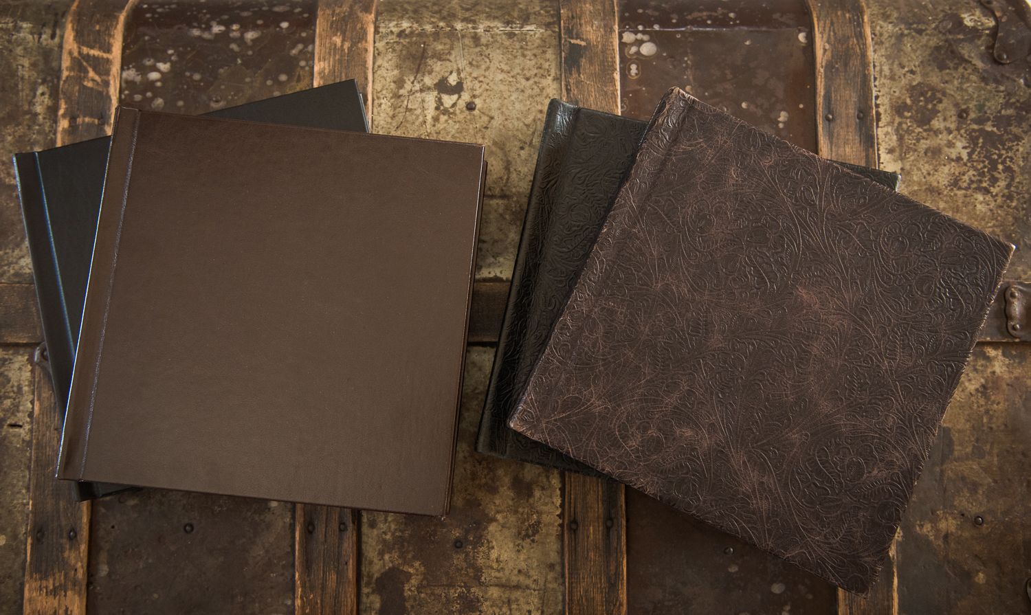 Four dark brown leather-bound books stacked on a rustic wooden surface.