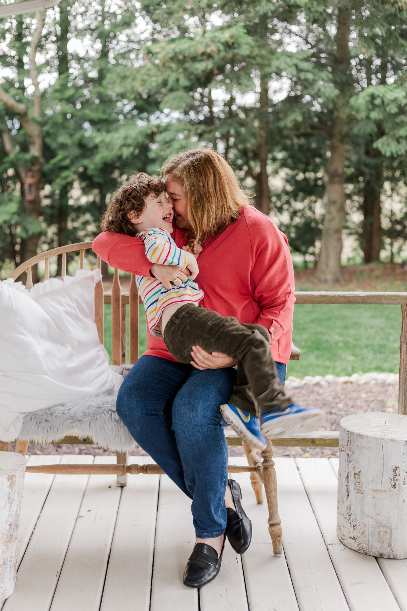 A mother and her son snuggling into each other while candidly laughing on a wooden bench on the front porch of a house in Ontario, Canada.