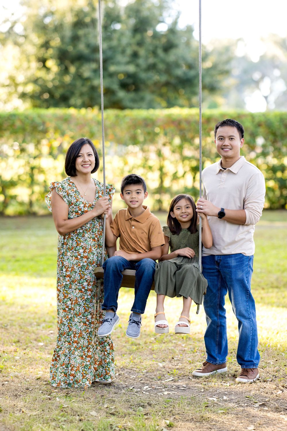 A family group poses together outdoors in a park setting during golden hour sunlight.