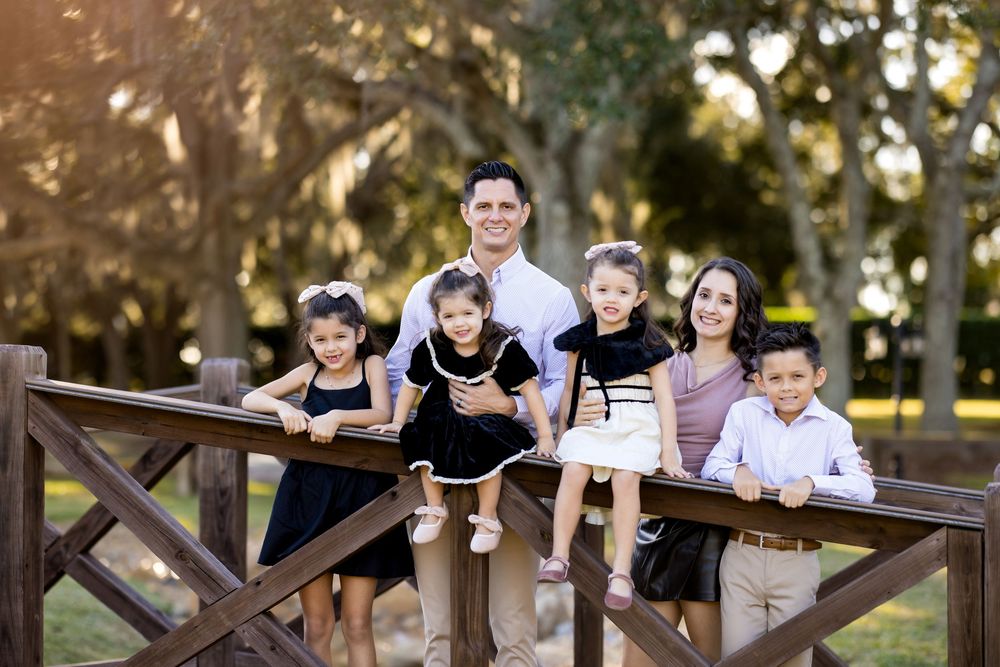 A group of children sit together on a wooden fence in a park during a sunny afternoon.