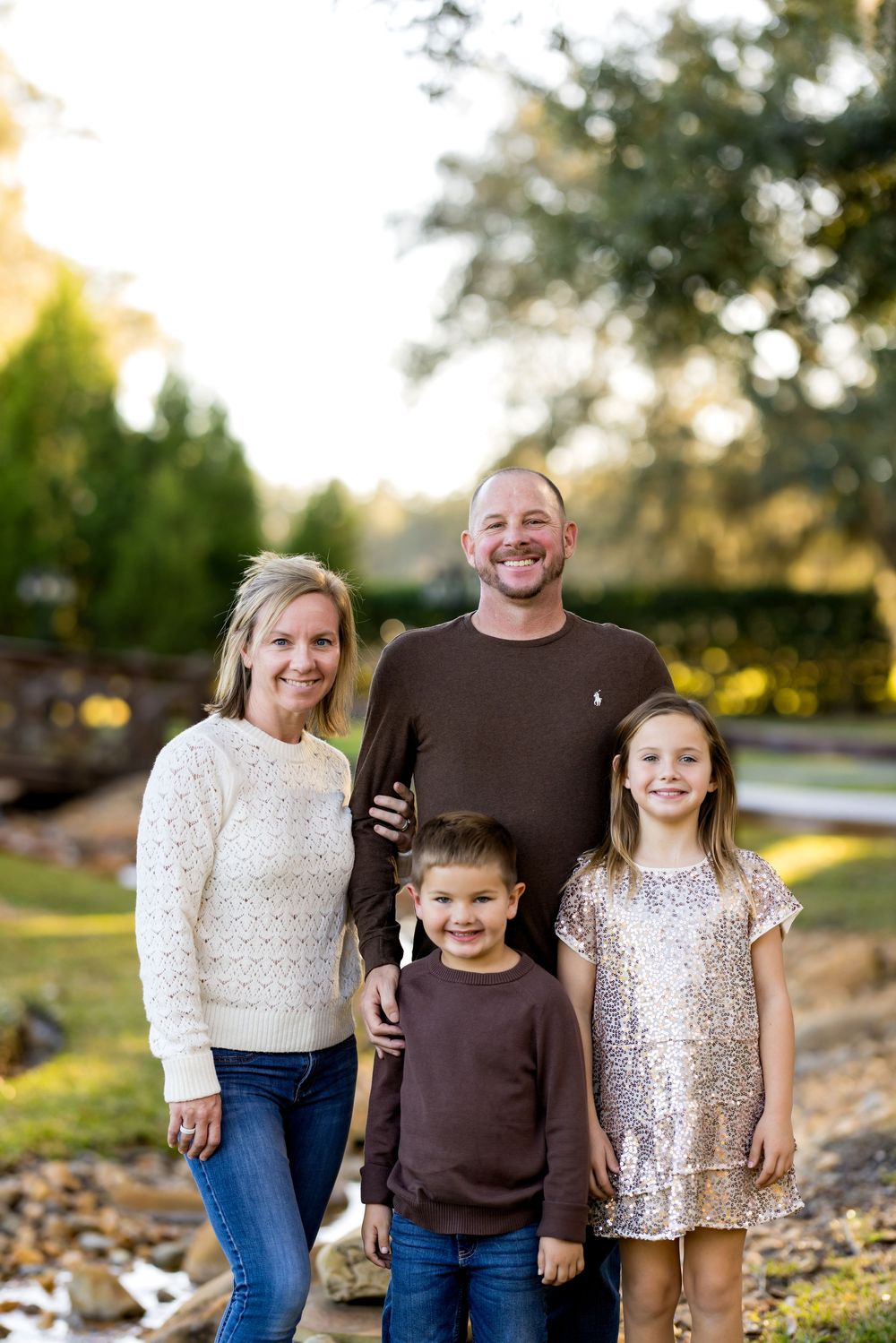 A family wearing coordinated brown and cream outfits poses together outdoors during golden hour.