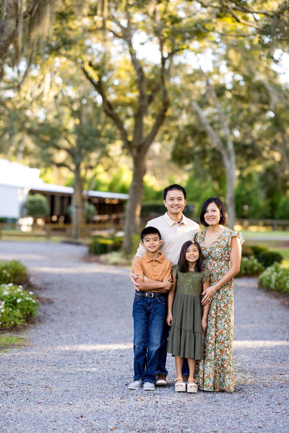 A family poses together on a gravel path surrounded by trees in a natural outdoor setting.