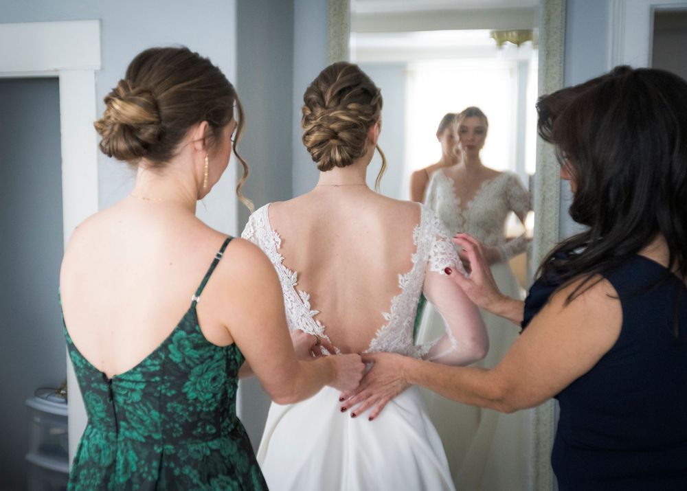 Wedding party members in green dresses and white gowns helping with preparations in a bright indoor space.