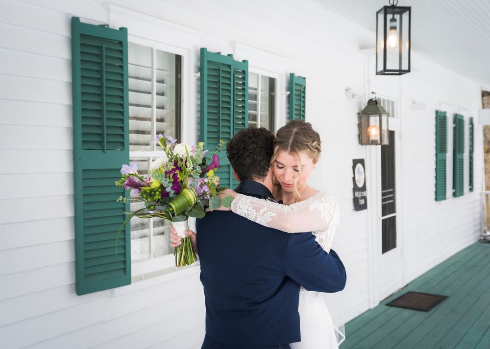 Couple embraces on a classic white porch with green shutters and hanging flower baskets.