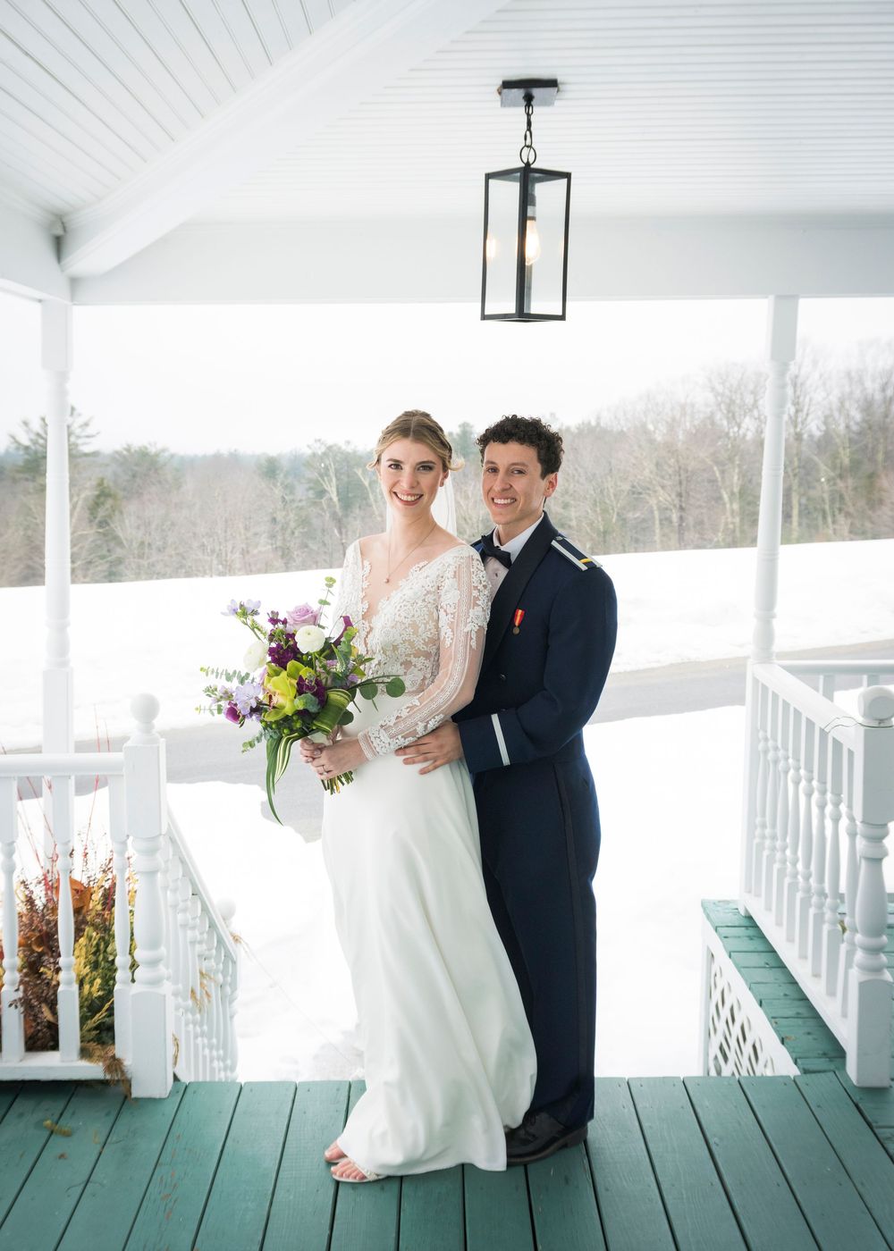 Wedding couple and wedding party pose together on a white wooden porch with floral decorations.