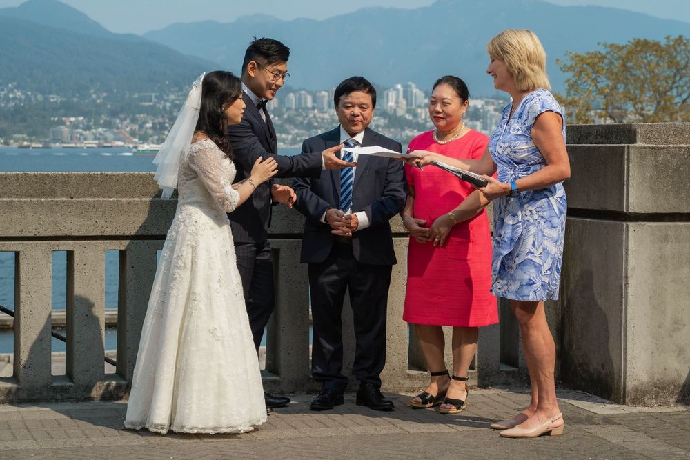 A small wedding gathering stands on a scenic overlook with mountains and water in the background.