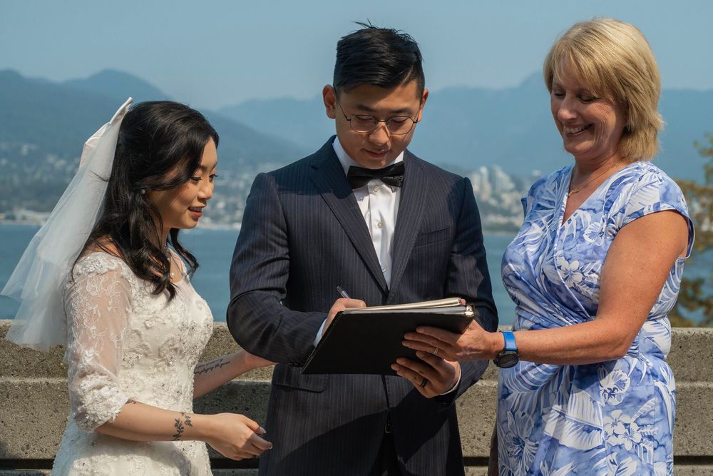 Outdoor wedding ceremony with officiant and couple against Vancouver skyline and mountains.