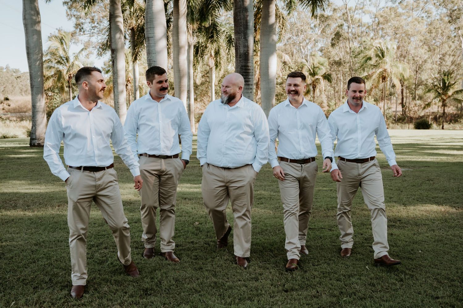 A group in coordinated light blue shirts and khaki pants pose together in a sunny outdoor gladstone garden setting.