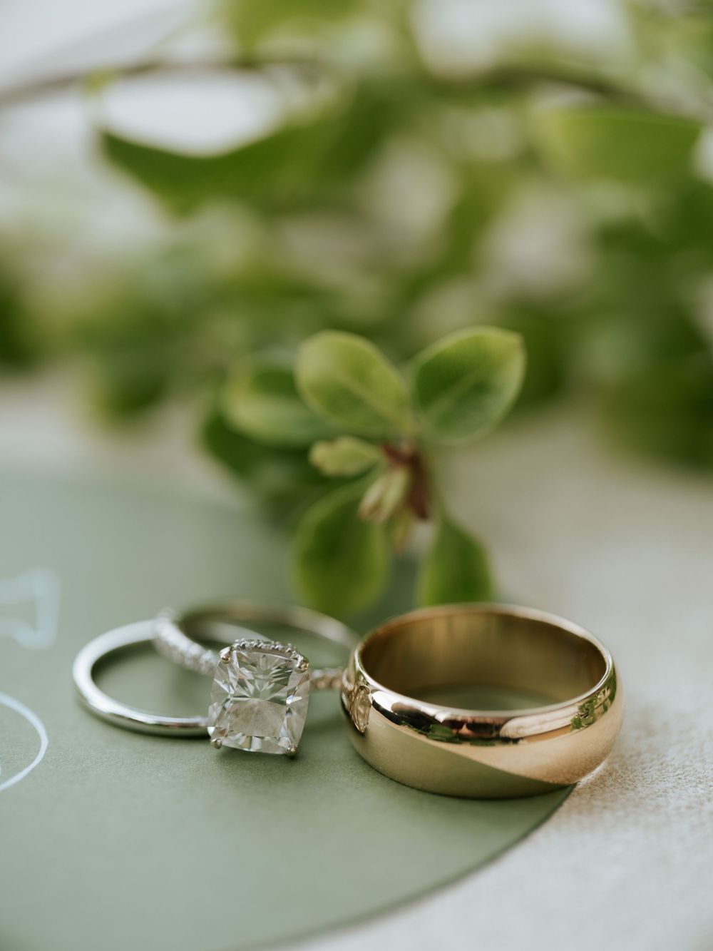 Wedding rings displayed on a soft green surface with natural light highlighting the diamond and metal bands.